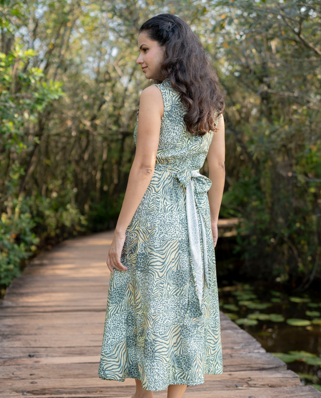 Woman in a green patterned dress standing on a wooden path with nature in the background
