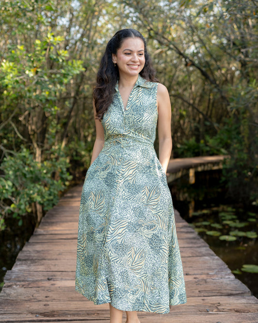 Woman in a green patterned dress standing on a wooden bridge with trees in the background
