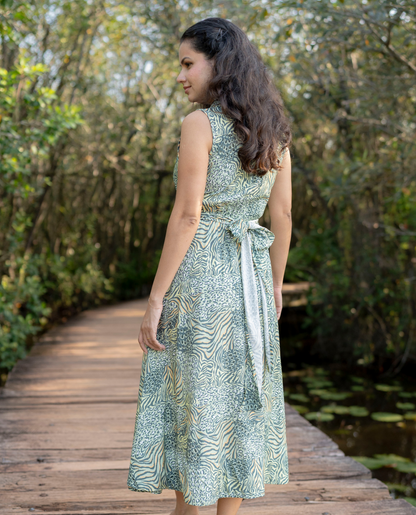 Woman in a green patterned dress standing on a wooden path with nature in the background
