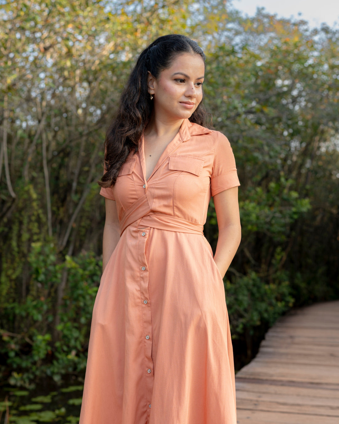 Woman in a peach dress standing outdoors with greenery in the background